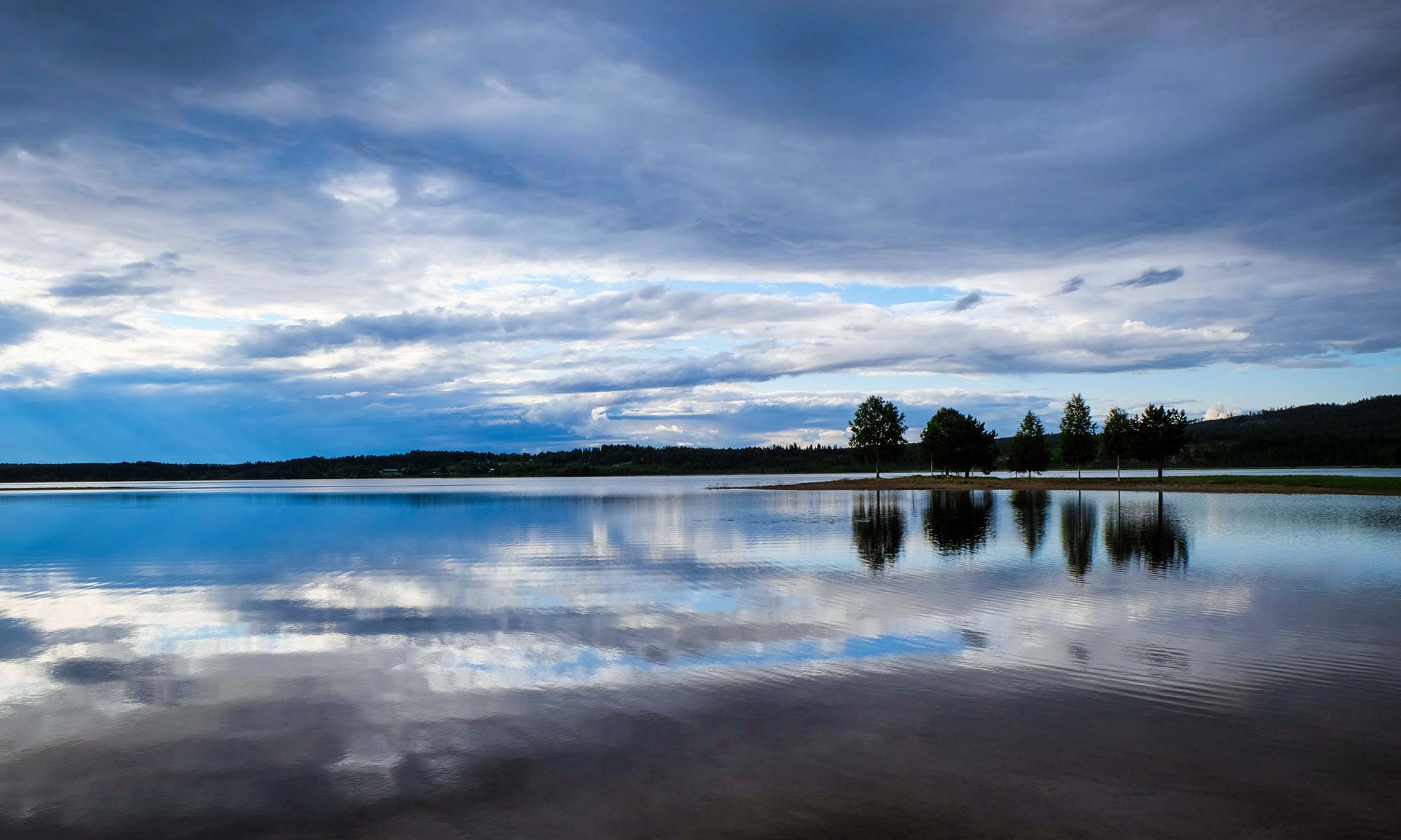 Reflektierender See. Reflektion von Bäumen und Wolken.